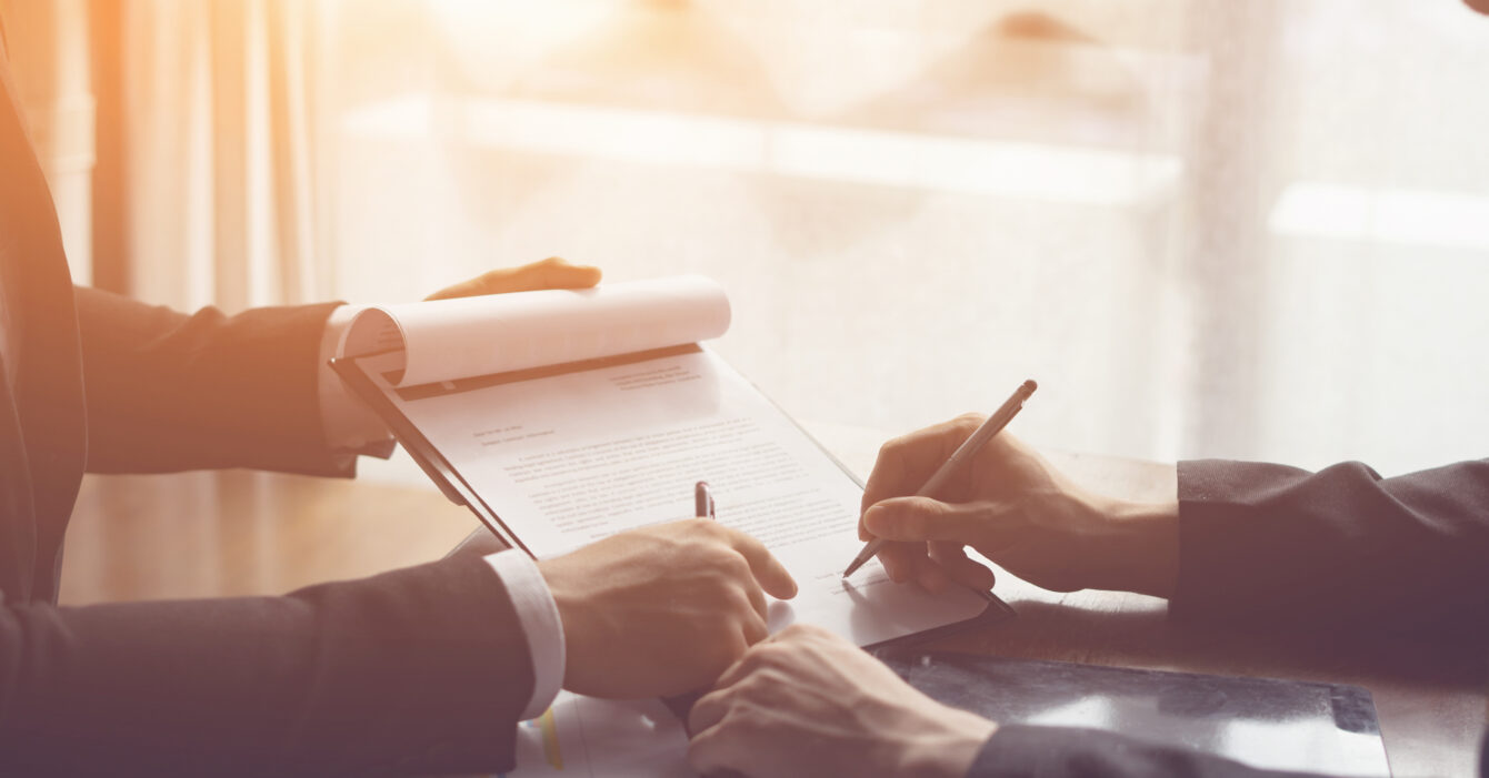 Businessperson Signing Contract about insurance, Two men writing with pen sign of modest agreements form In modern office, morning light, vintage color, success of business partners concept